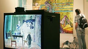 Ein Ausstellungsbesucher betrachtet eine Raum-Installation der Künstlergruppe Artists Anonymous, bei der Monitore ins Negativ verkehrte Bilder zeigen.